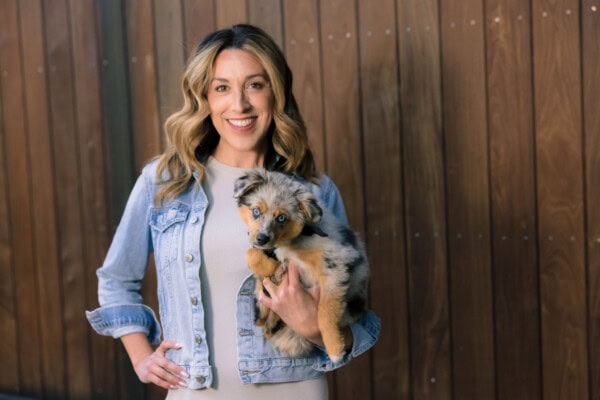 Woman with brown hair, wearing denim jacket holding a puppy.